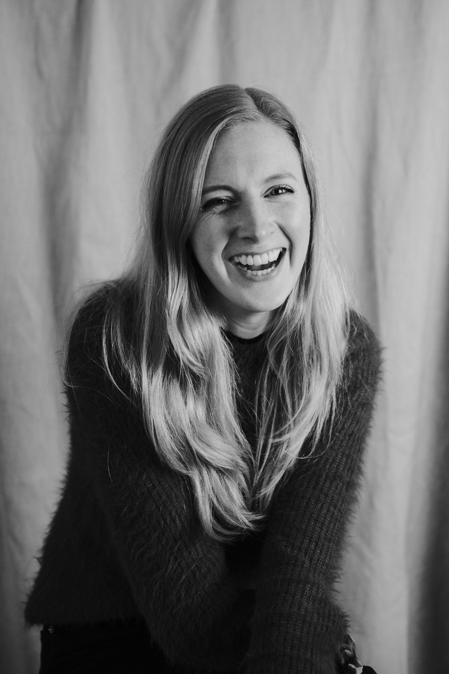 Black and white portrait of a person laughing while wearing a dark sweater against a light backdrop.
