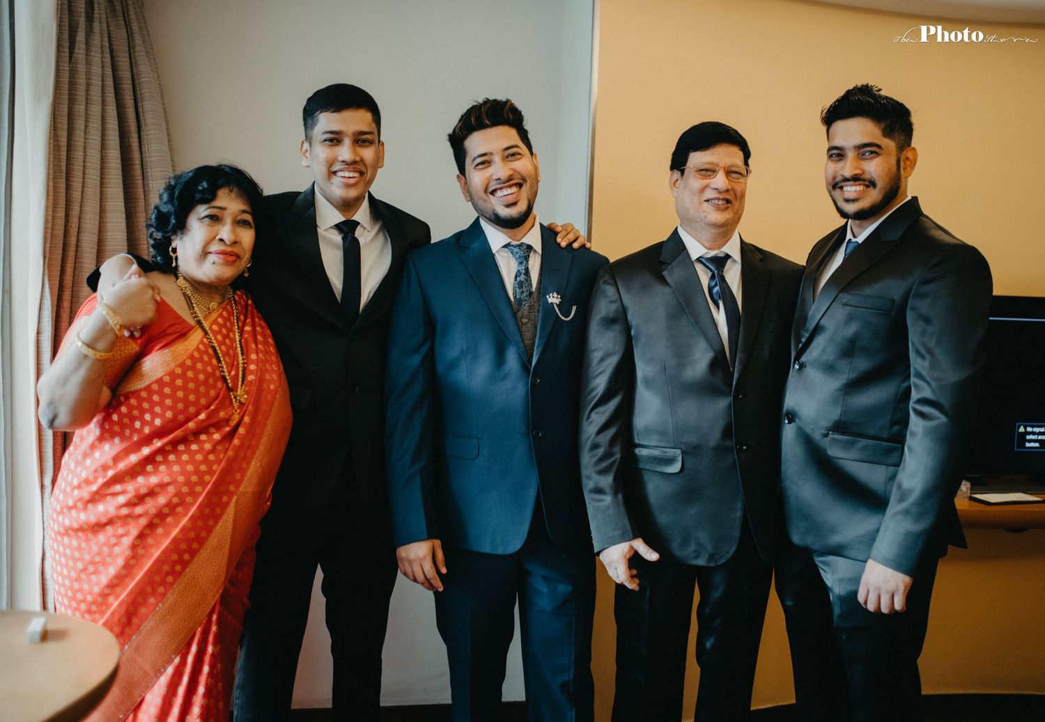 Wedding party members in formal suits posing together in a hotel room.