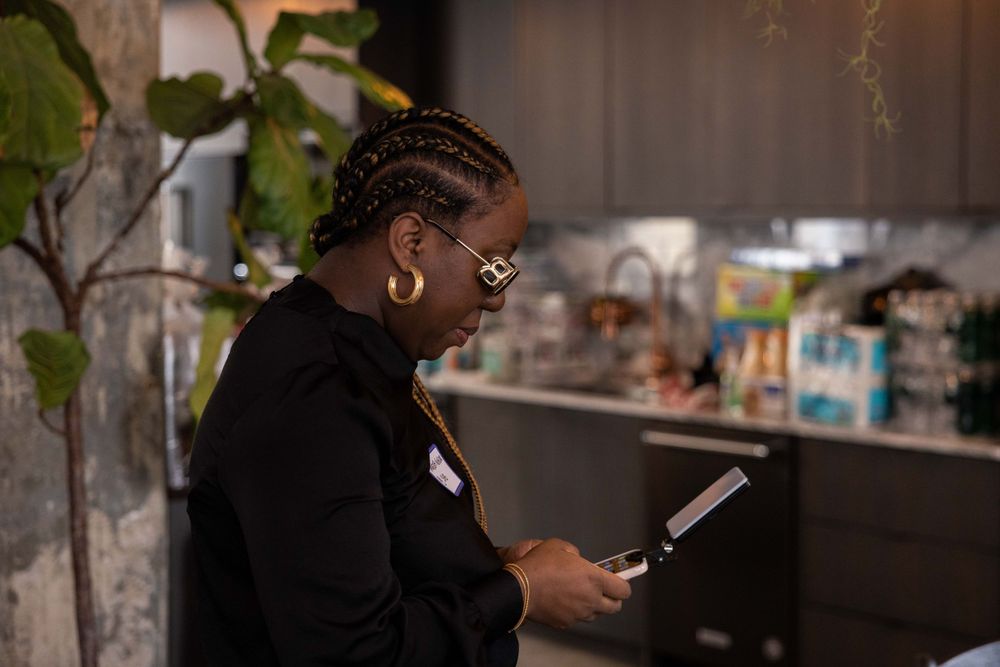 Person in a black outfit checking their phone while standing by a counter.