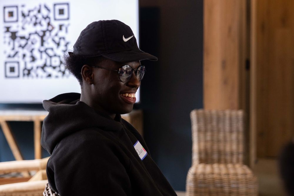 Person in a black Nike cap and dark hoodie looking to the side in an indoor setting.