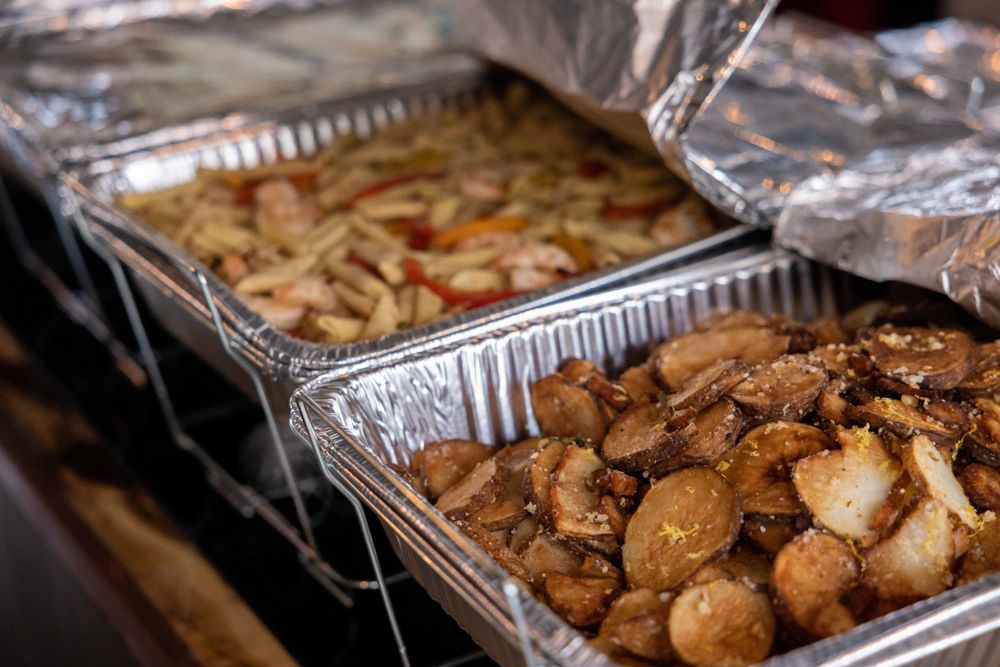 Two aluminum catering trays filled with cooked meat and pasta dishes.
