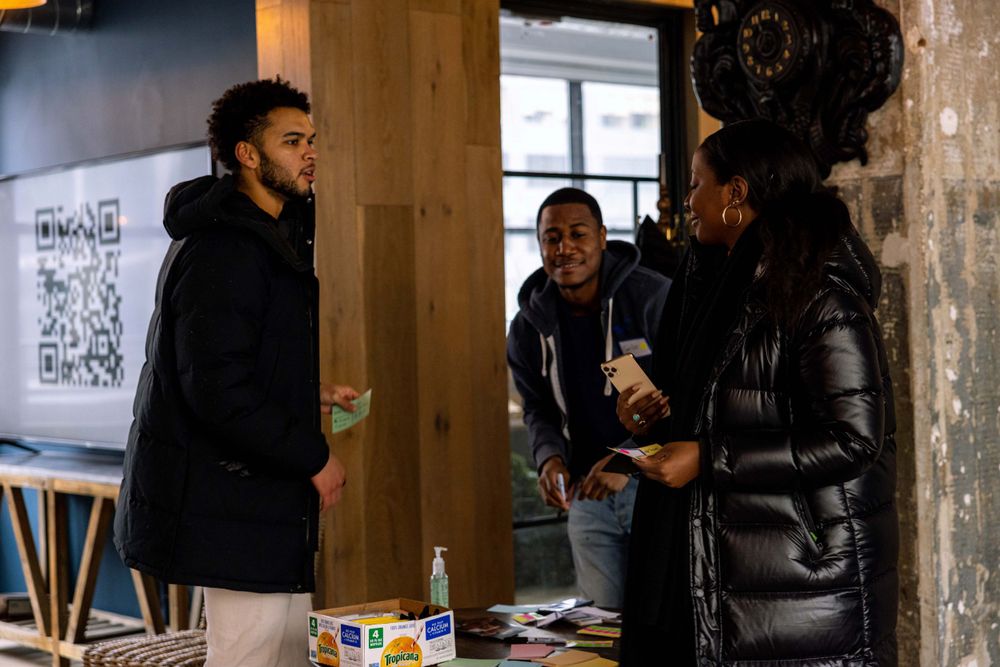 Three people engaged in conversation near a wall with QR codes.