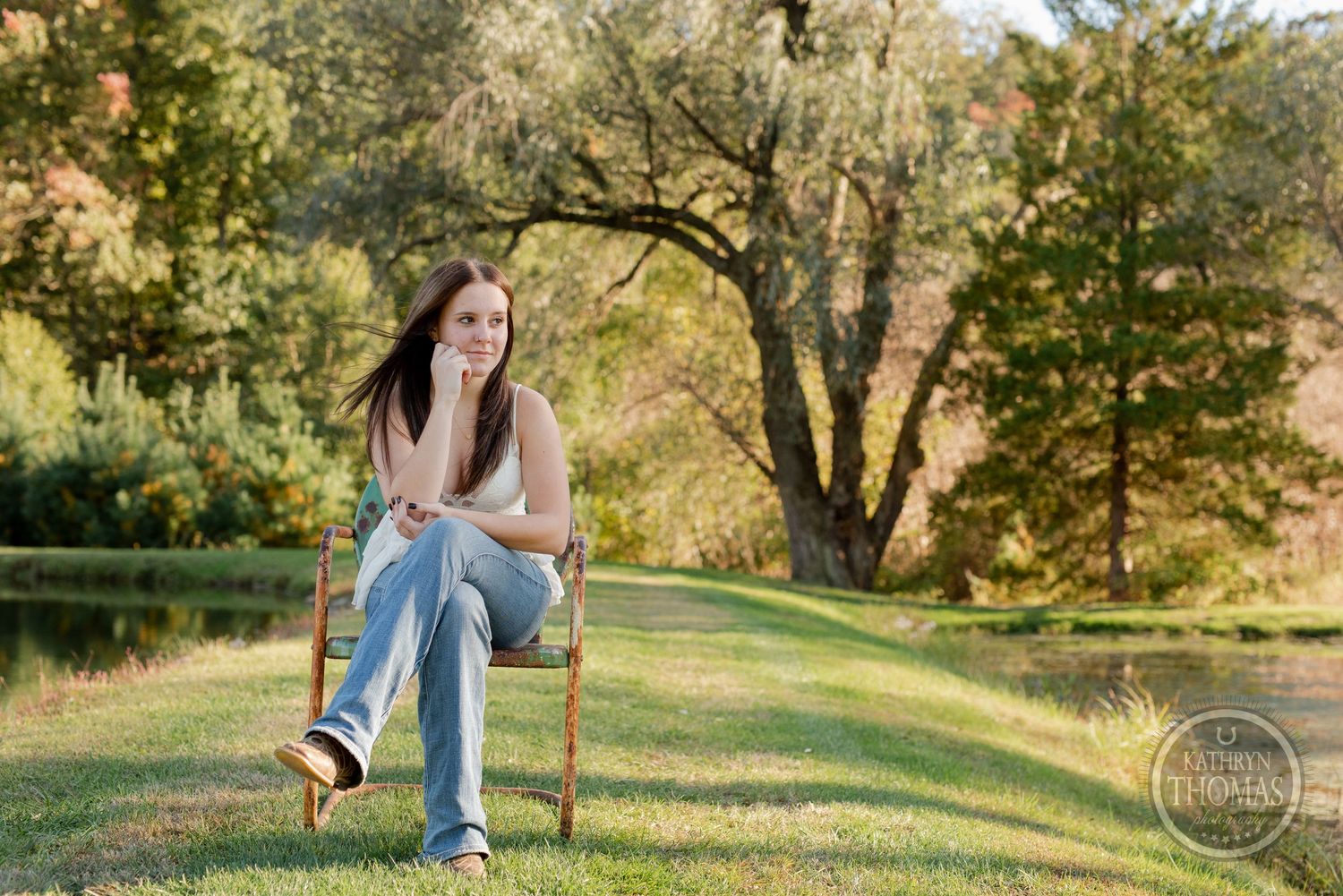 Outdoor portrait sitting on vintage chair with autumn trees in background.