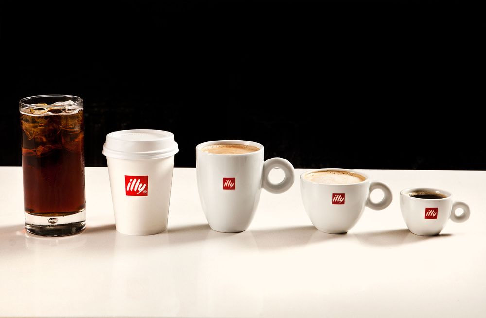 Different sizes of illy coffee cups and glasses arranged in ascending order against a black background.
