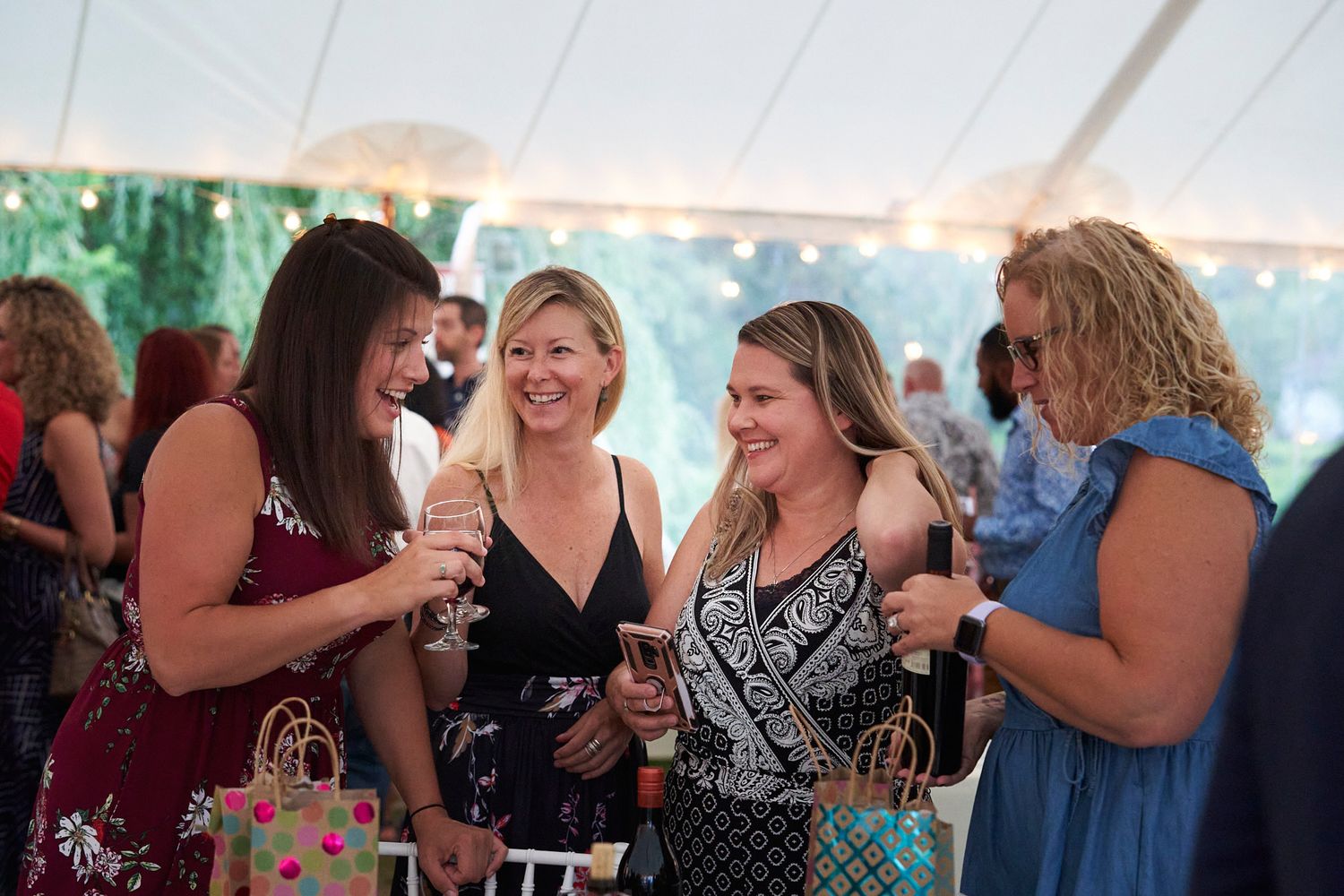 Group of women chatting and laughing at an outdoor party event under a white tent.