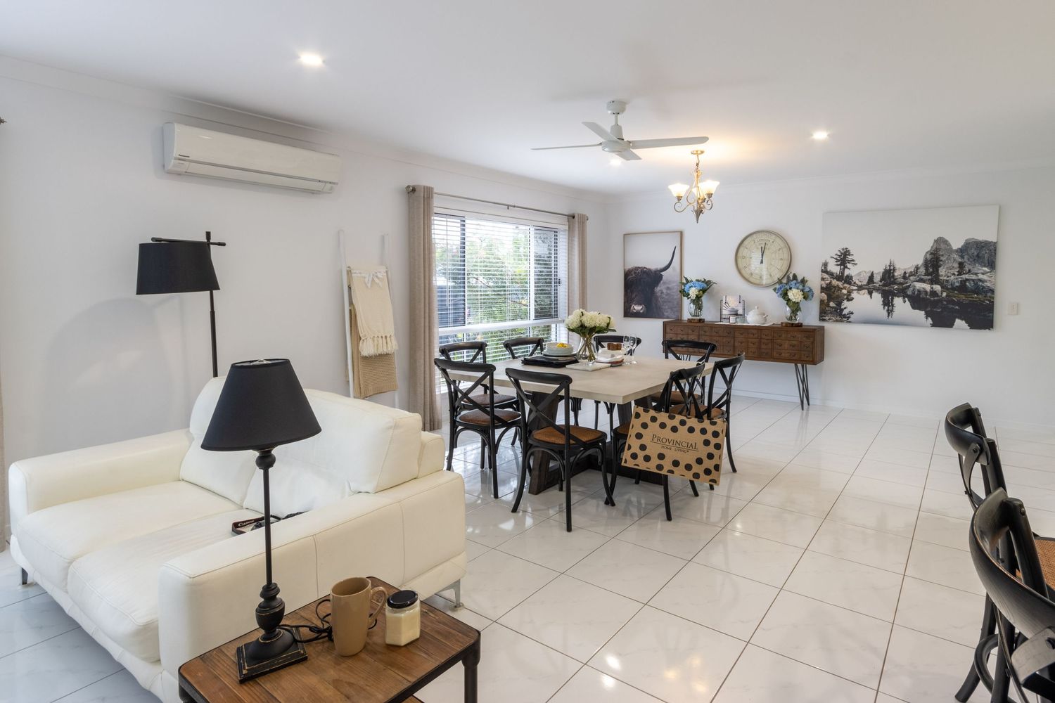 Modern open plan living room with white sofa, dining area and tiled flooring.