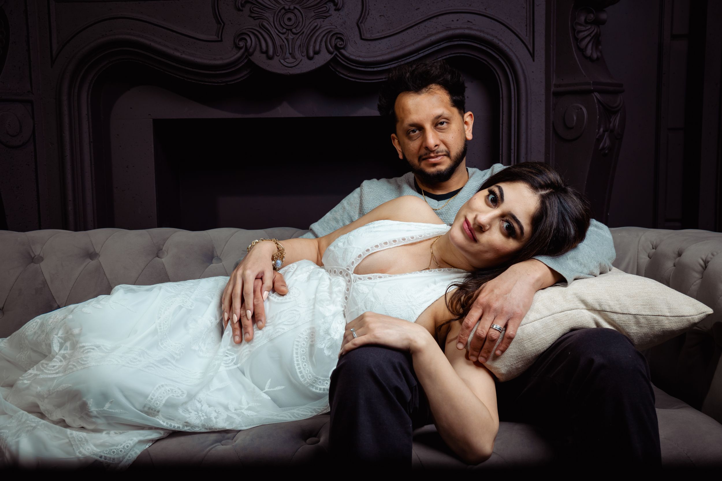 Dramatic indoor couple portrait session with vintage furniture and dark moody lighting.
