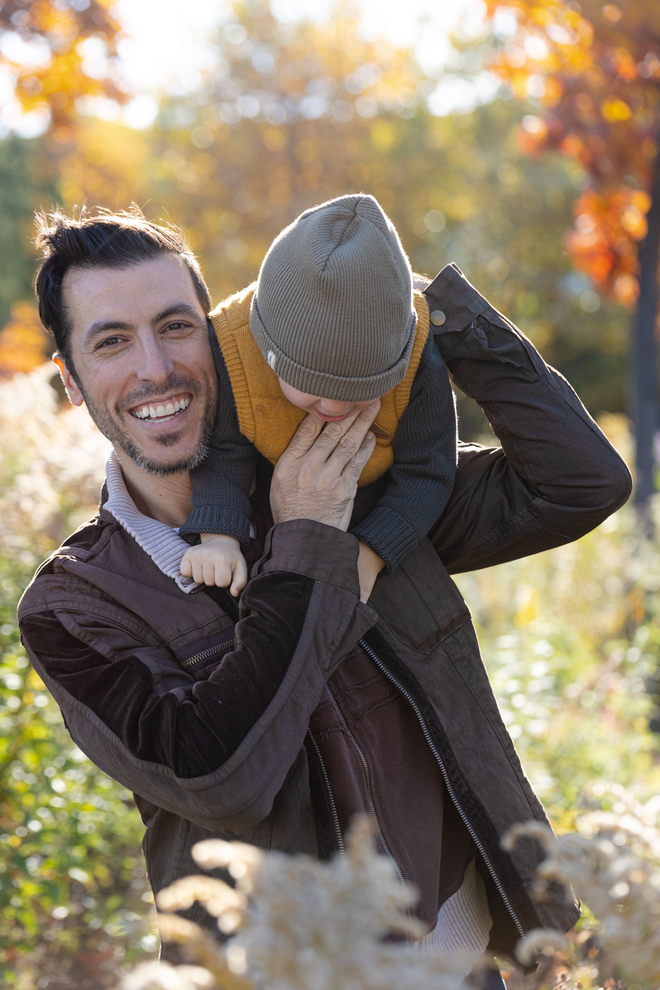 Father and child share playful moment in autumn foliage with golden sunlight.