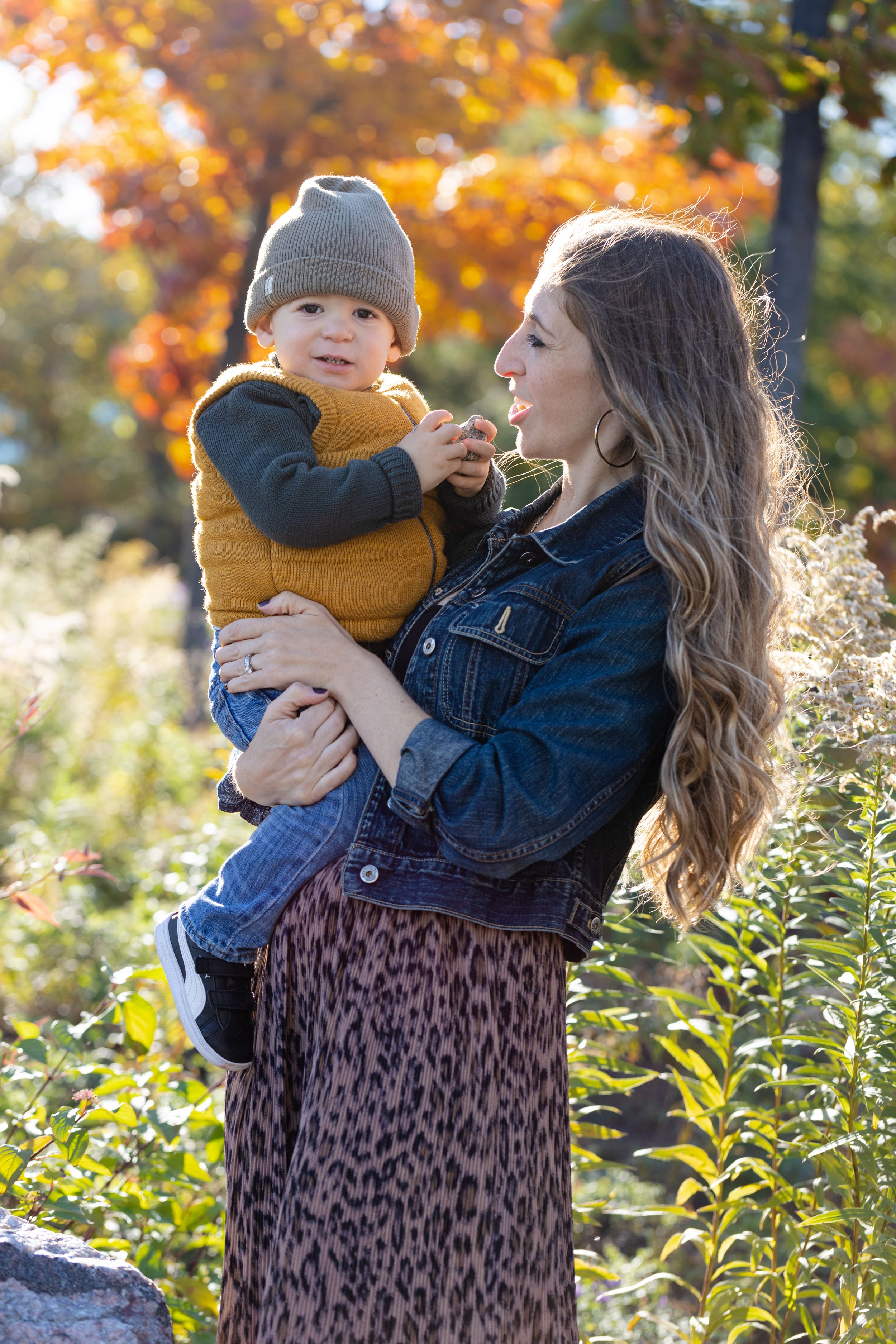 Parent and child sharing tender moments outdoors in autumn with golden foliage in the background.