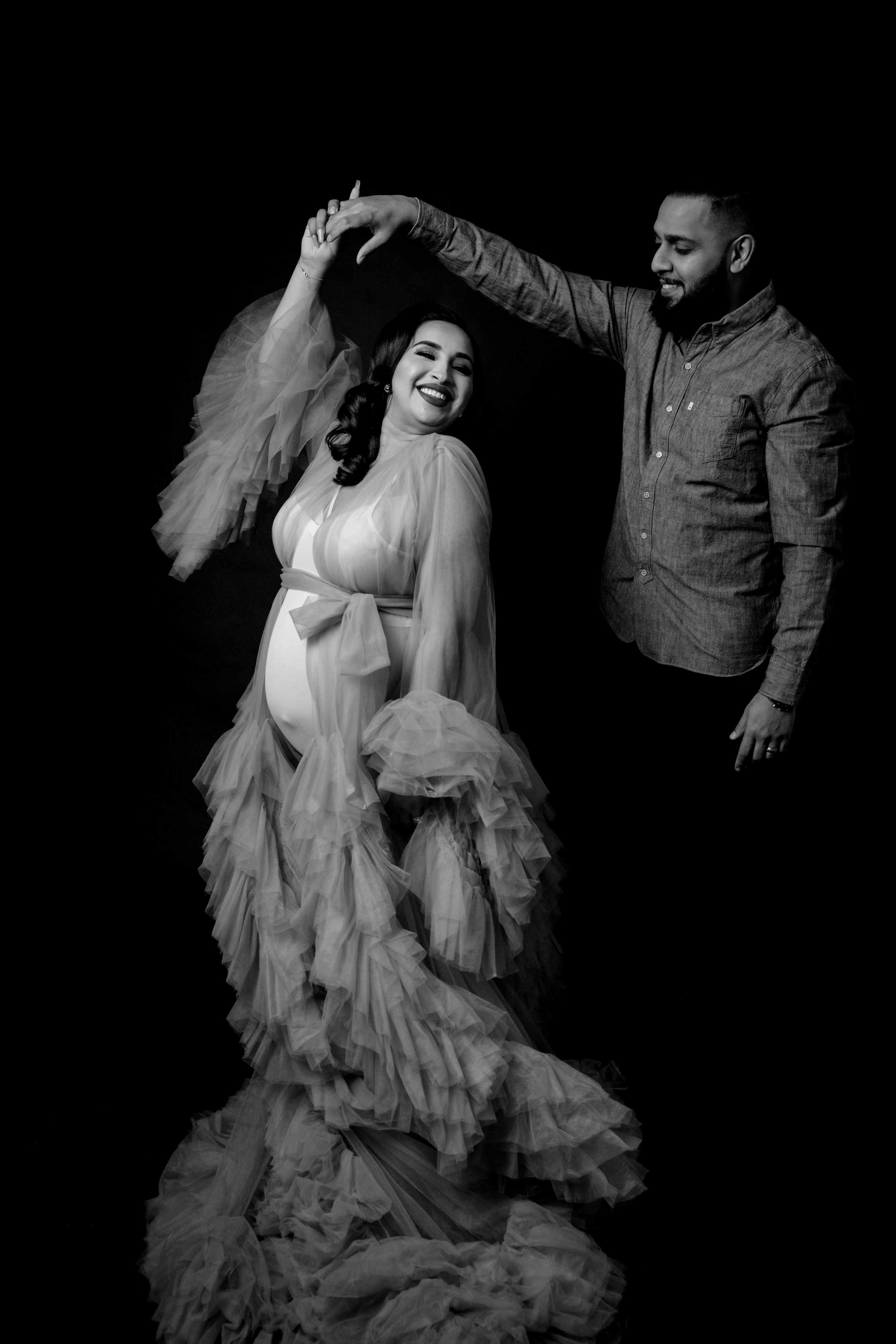 Artistic black and white maternity session showing joyful moments in flowing dress.