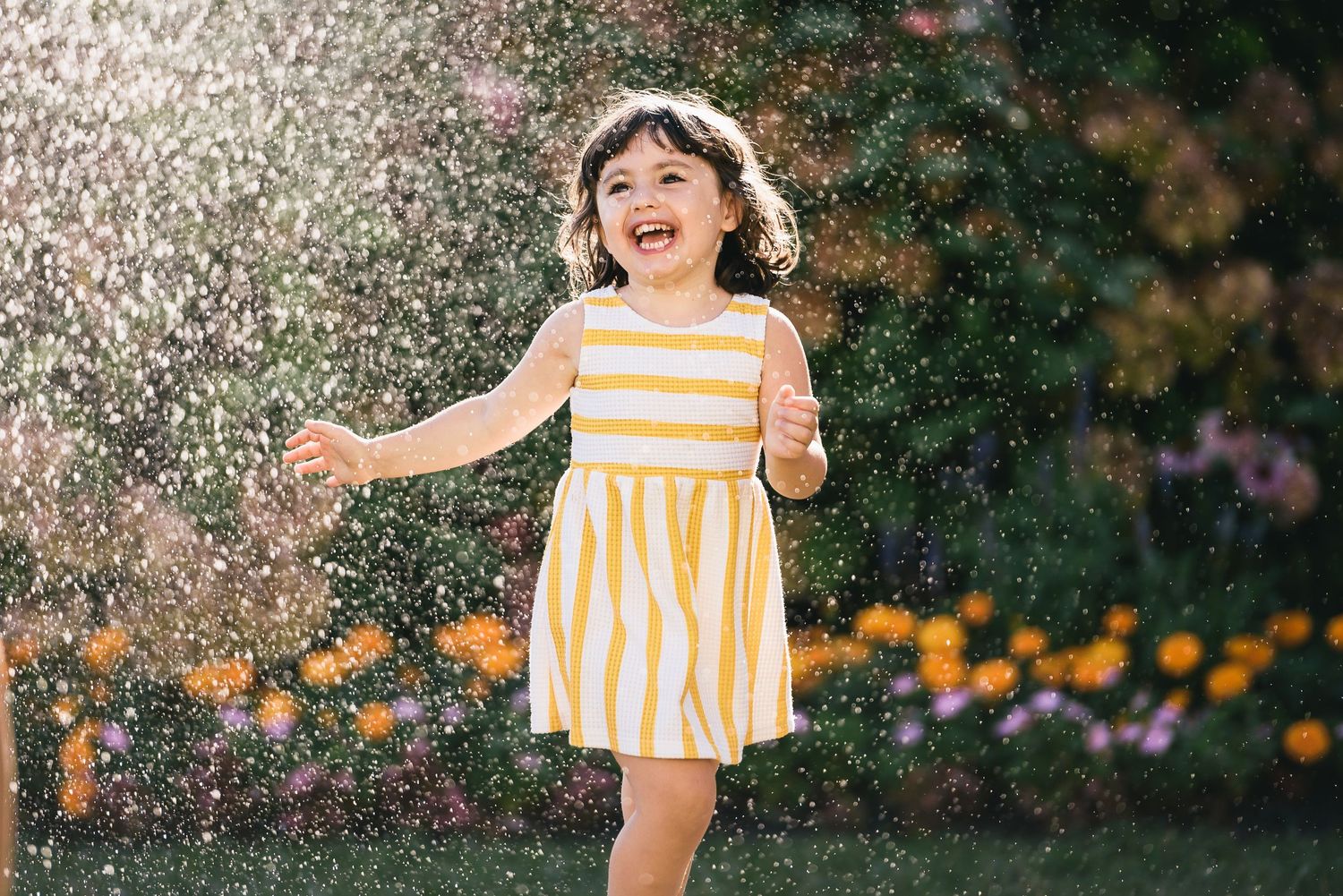 A joyful scene of a yellow striped summer dress in a garden with water droplets spraying in the sunlight.