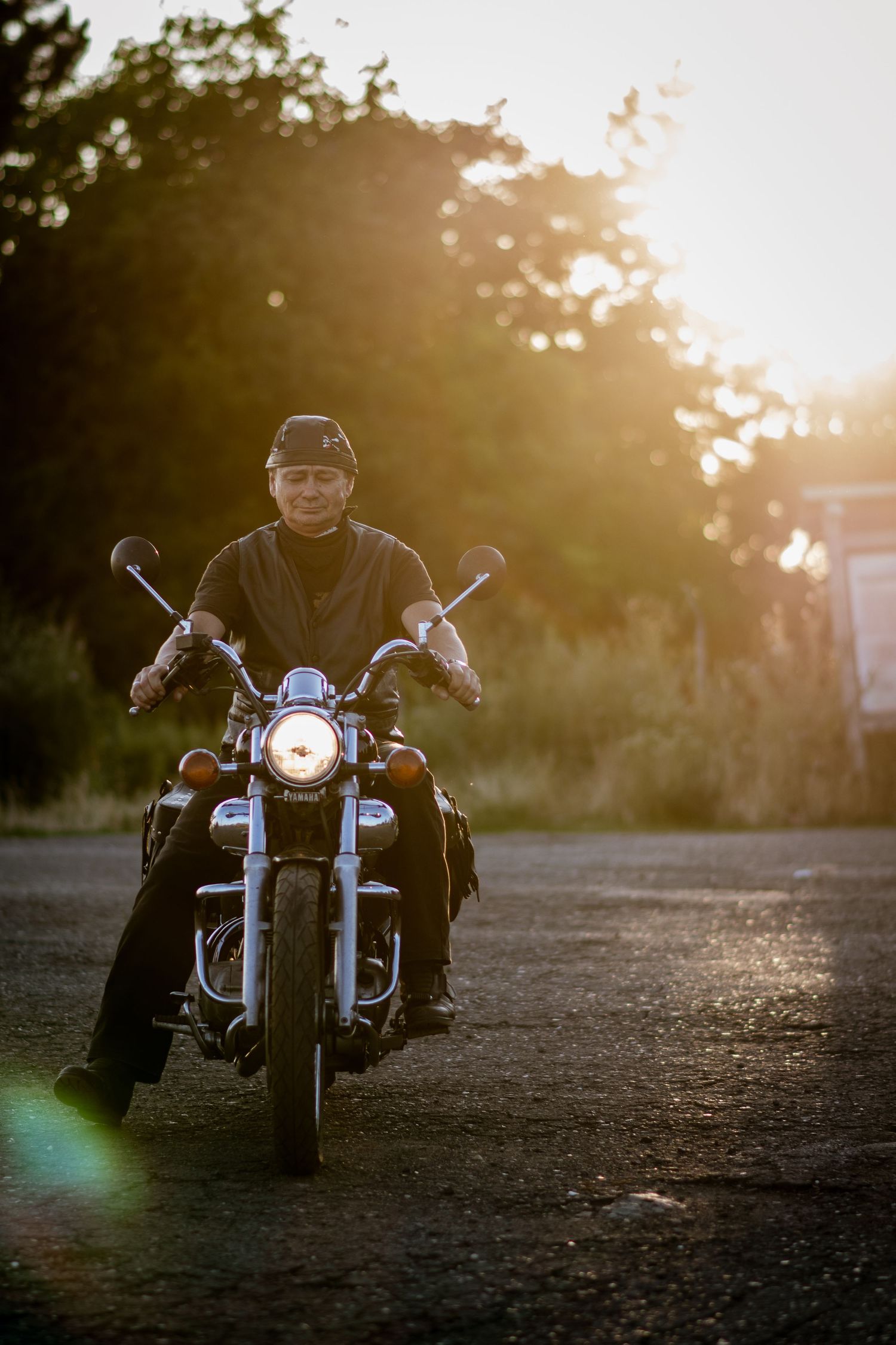 Person riding motorcycle at golden hour with sun flare and natural backdrop.