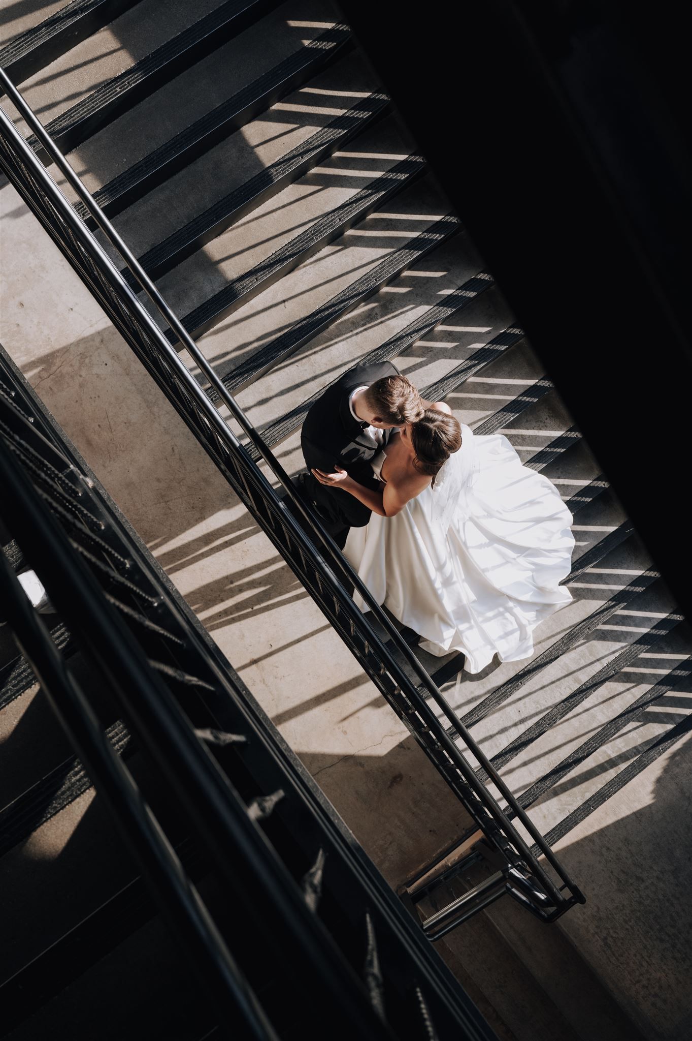 A dramatic overhead view of a couple sharing a moment on a black staircase with striking shadows.
