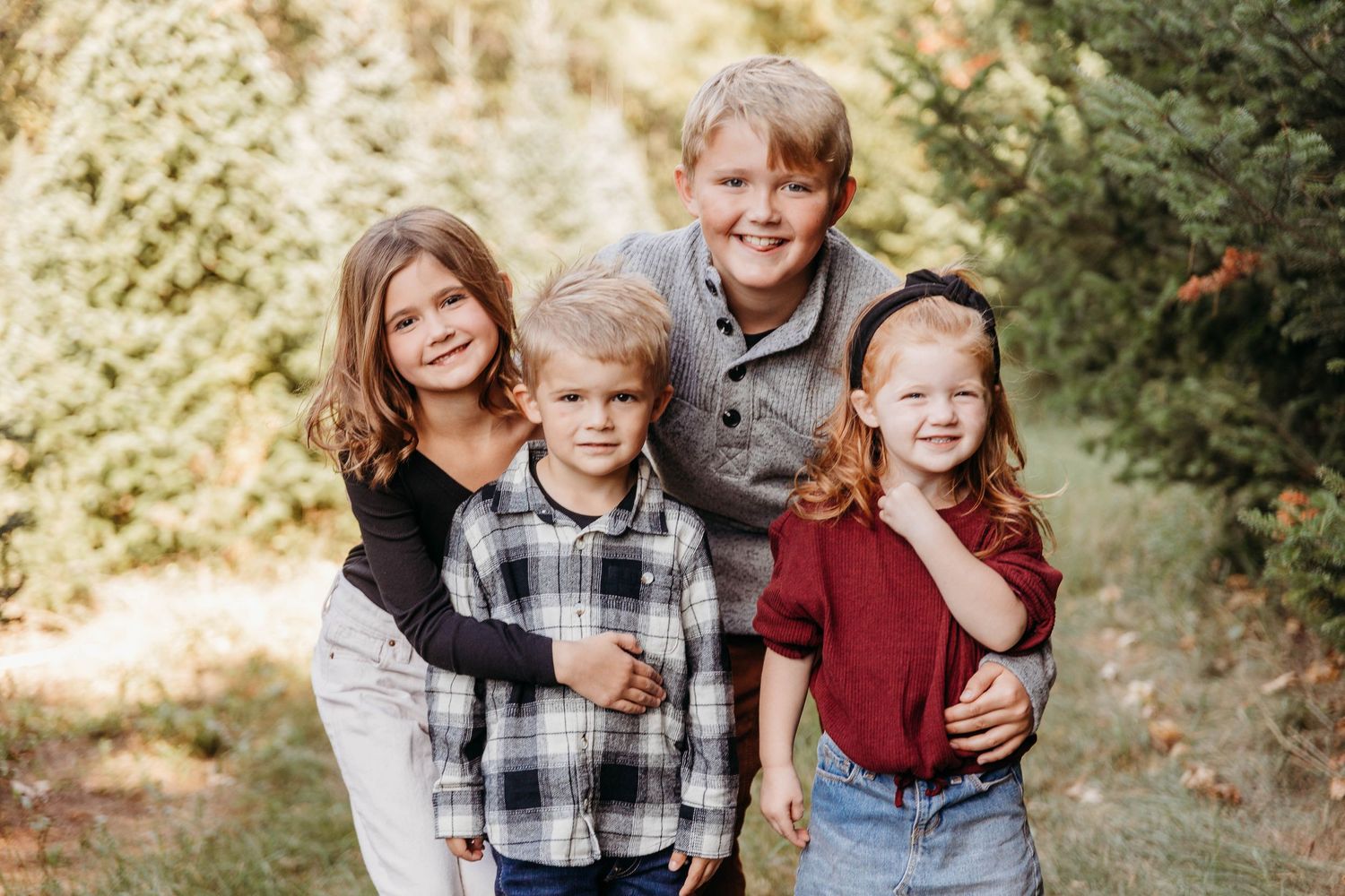 A family poses together outdoors during an autumn photo session wearing coordinated casual outfits in plaid and burgundy.