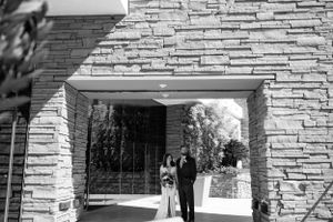 A wedding couple stands beneath a stone archway entrance.