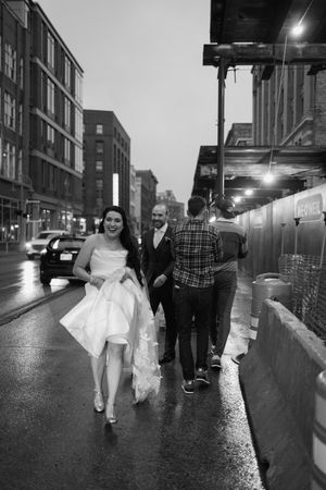 A couple walks down a rainy city street after their wedding with the bride lifting her gown.