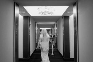 A bride in a white dress walks down a modern hotel hallway with dramatic lighting.