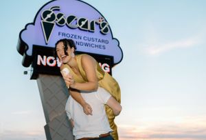 A playful couple poses in front of an ice cream shop sign at sunset.