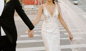 Bride and groom holding hands while crossing city street in elegant wedding attire.