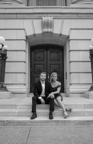 Couple in formal wear sitting on grand stone steps with classic architecture in background.