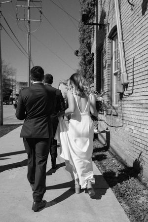 Black and white photo of couple walking down sidewalk past brick building on sunny day.