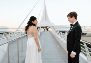 A couple in formal attire stands on a modern white bridge during their wedding photoshoot.