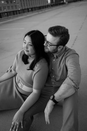 A couple shares an intimate moment while sitting on a concrete surface in black and white.