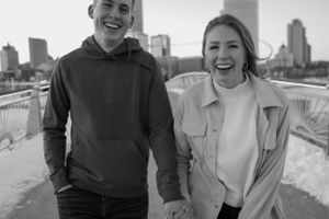 Happy couple laughing together on bridge with city skyline in background.
