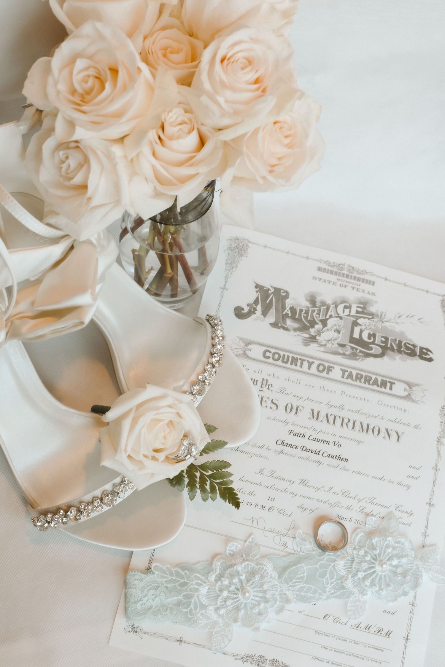 Wedding details with blush roses, marriage license, and delicate jewelry on a light background.