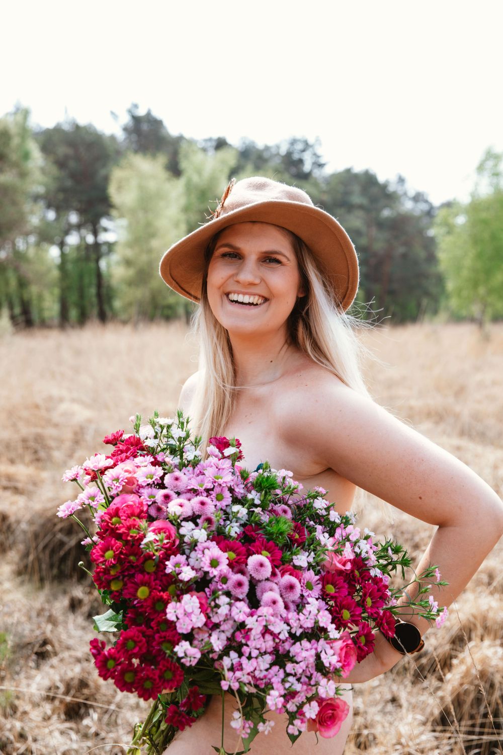 Woman in sun hat holds vibrant bouquet of pink and red flowers in outdoor setting.