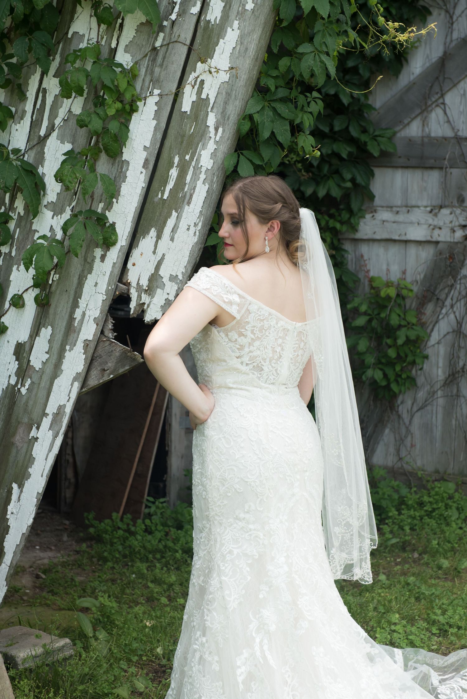 A bride in a lace wedding dress poses elegantly among white birch trees in a garden setting.