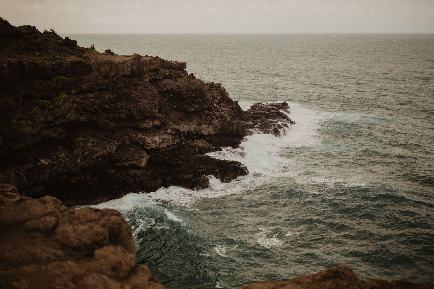Dramatic rocky coastline with waves crashing against cliffs in moody lighting.