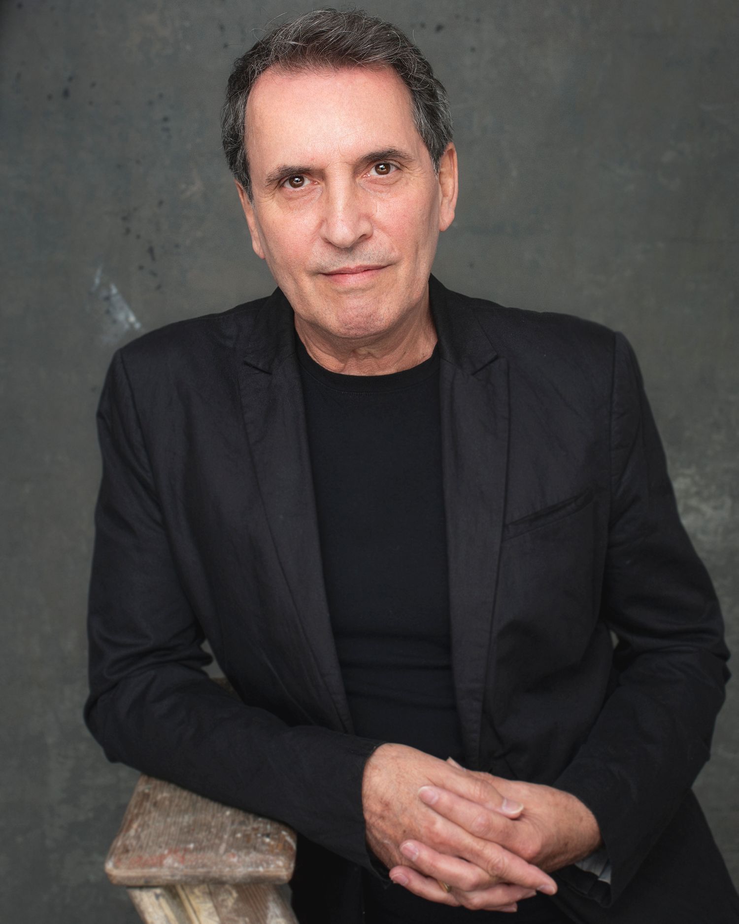 Professional studio portrait of mature man in black blazer and shirt against grey backdrop.