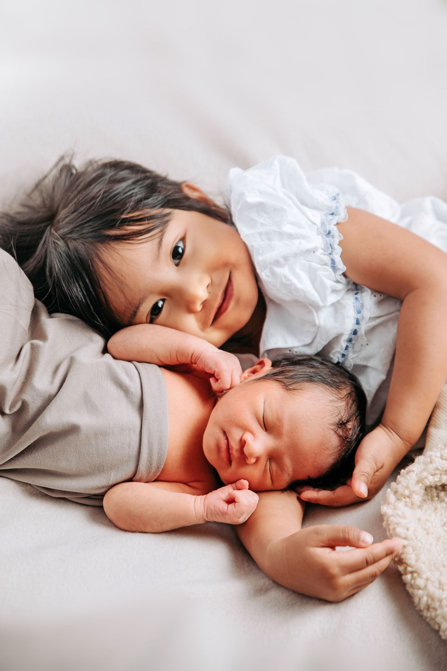Two siblings sharing a tender moment while resting on soft bedding.