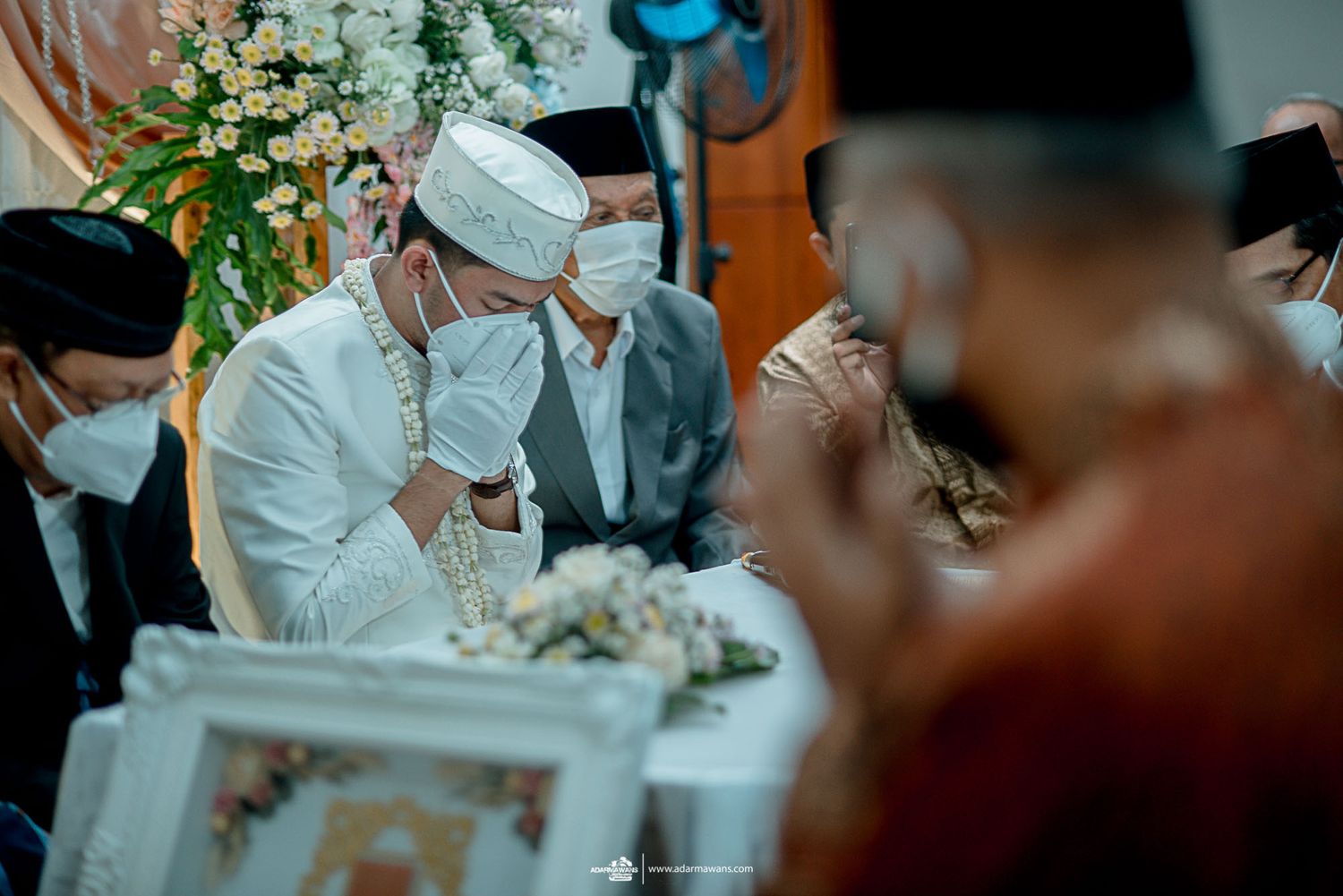 Religious ceremony participant in white attire and mask during emotional moment.