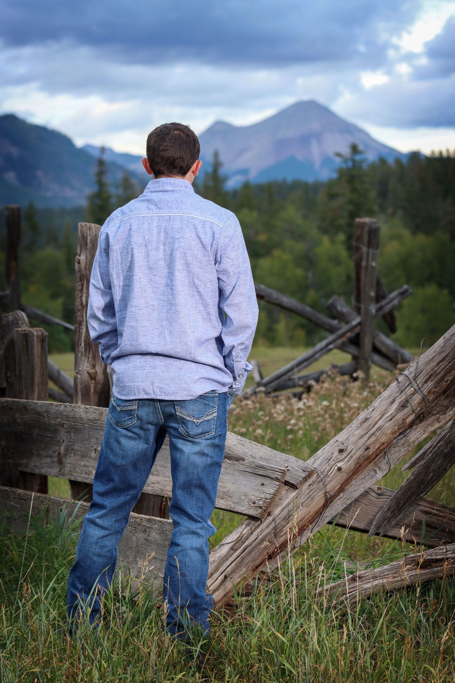 Person in light sweater looks out at mountain landscape while standing by wooden fence.