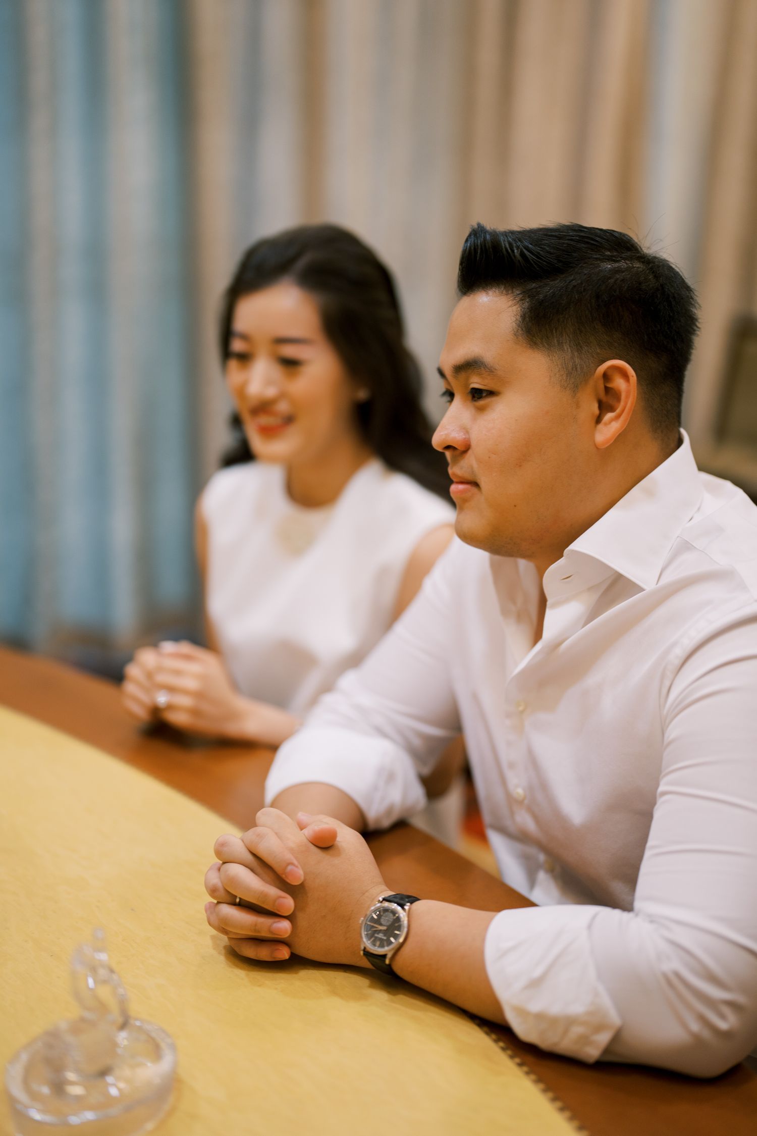 Two people in white attire sitting at a wooden table in a meeting room.
