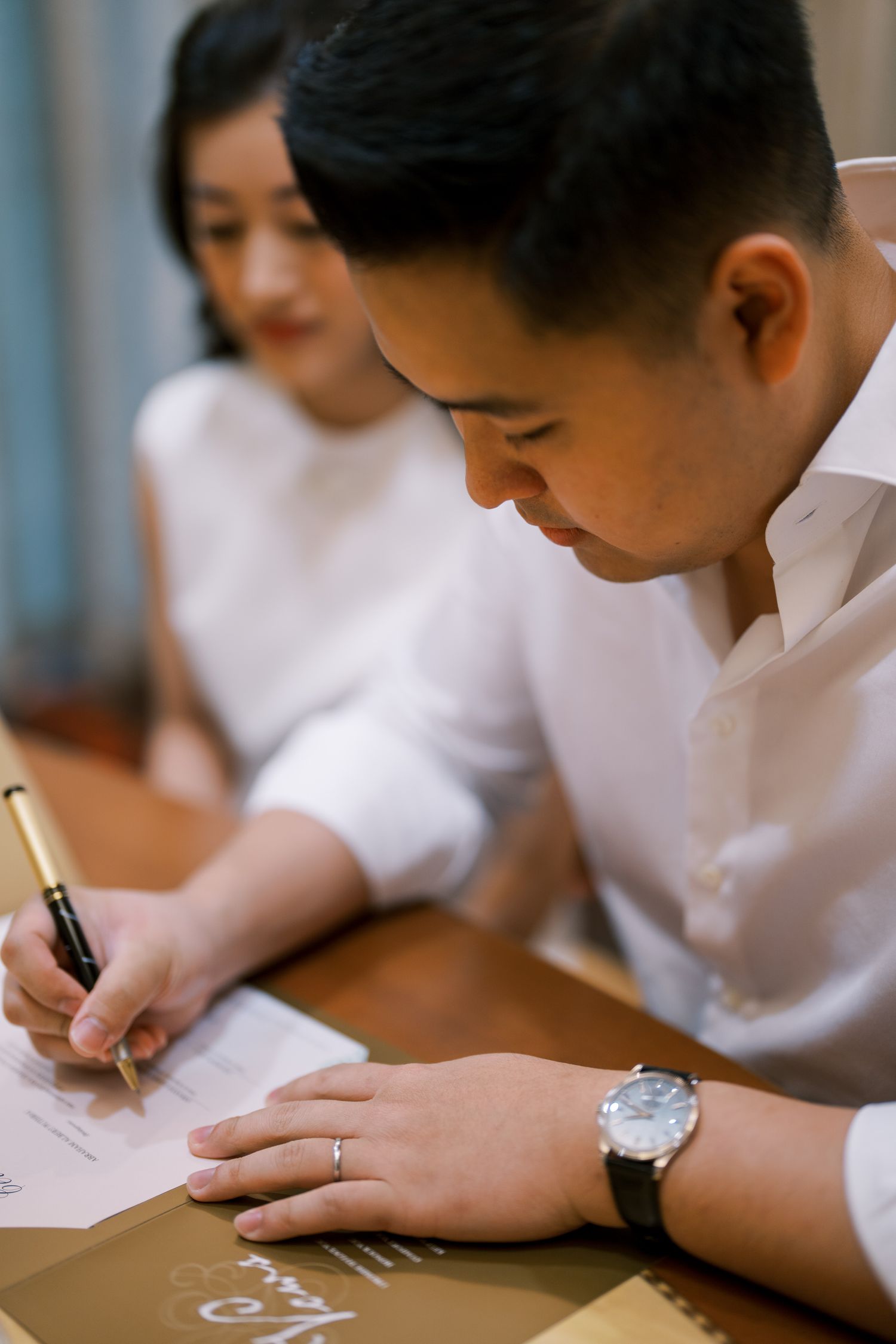 Close-up view of someone in a white shirt writing on a document at a wooden table.