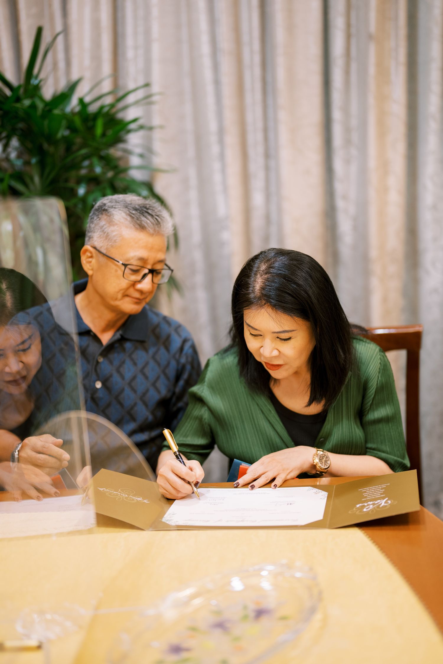 People seated at a table signing documents with a curtained background.