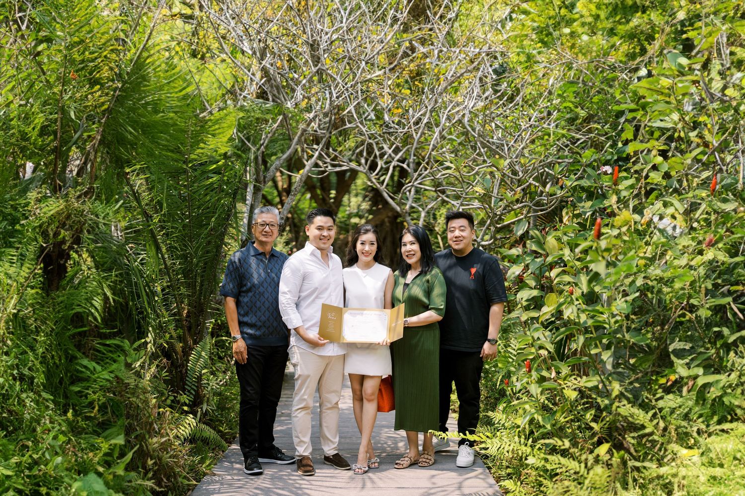 A group of people gathered outdoors in a garden pathway surrounded by greenery.