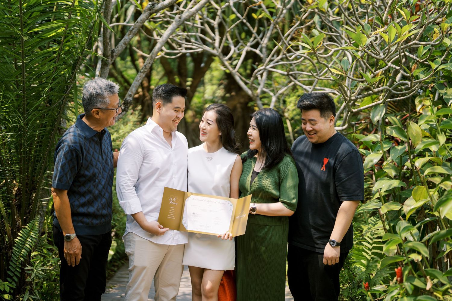 Outdoor group gathering with people holding documents among green vegetation.