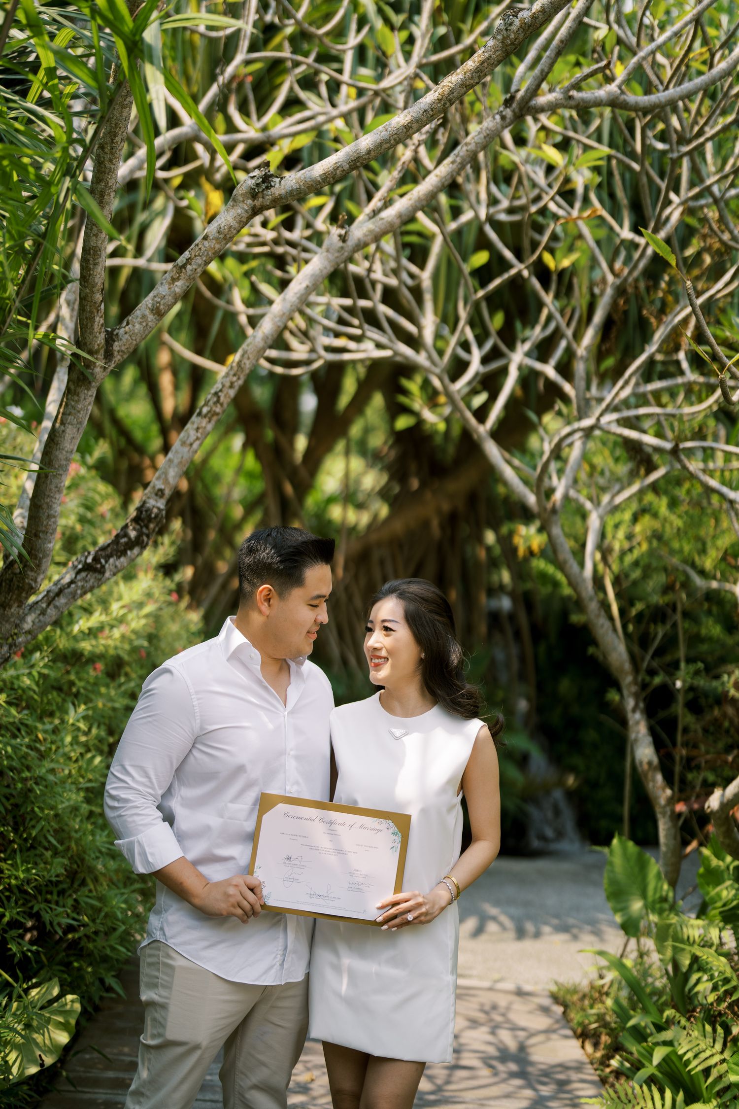 A joyful moment captured between two people in white attire under tree branches.