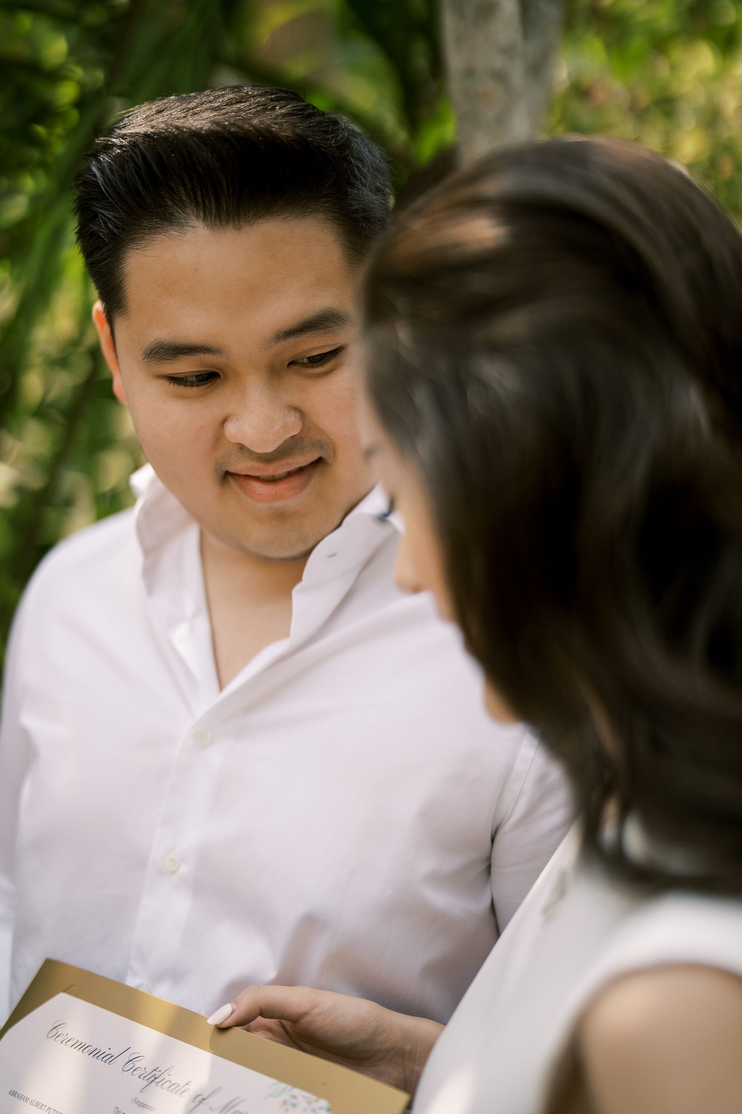 Two people in white clothing sharing a tender moment while looking at a document together.