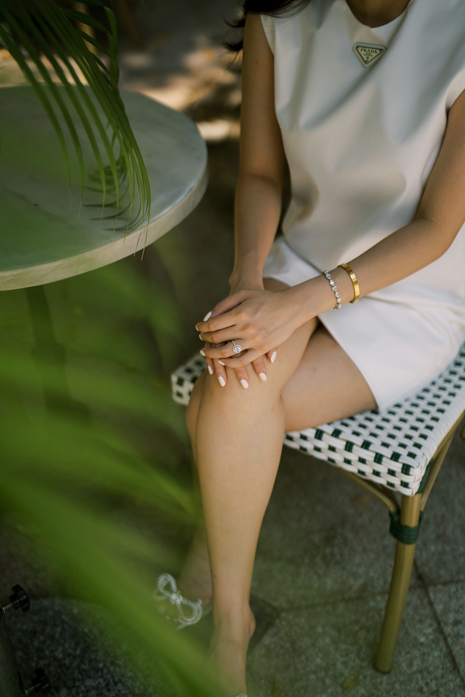Close-up of someone in white sitting on a patterned chair with jewelry details.