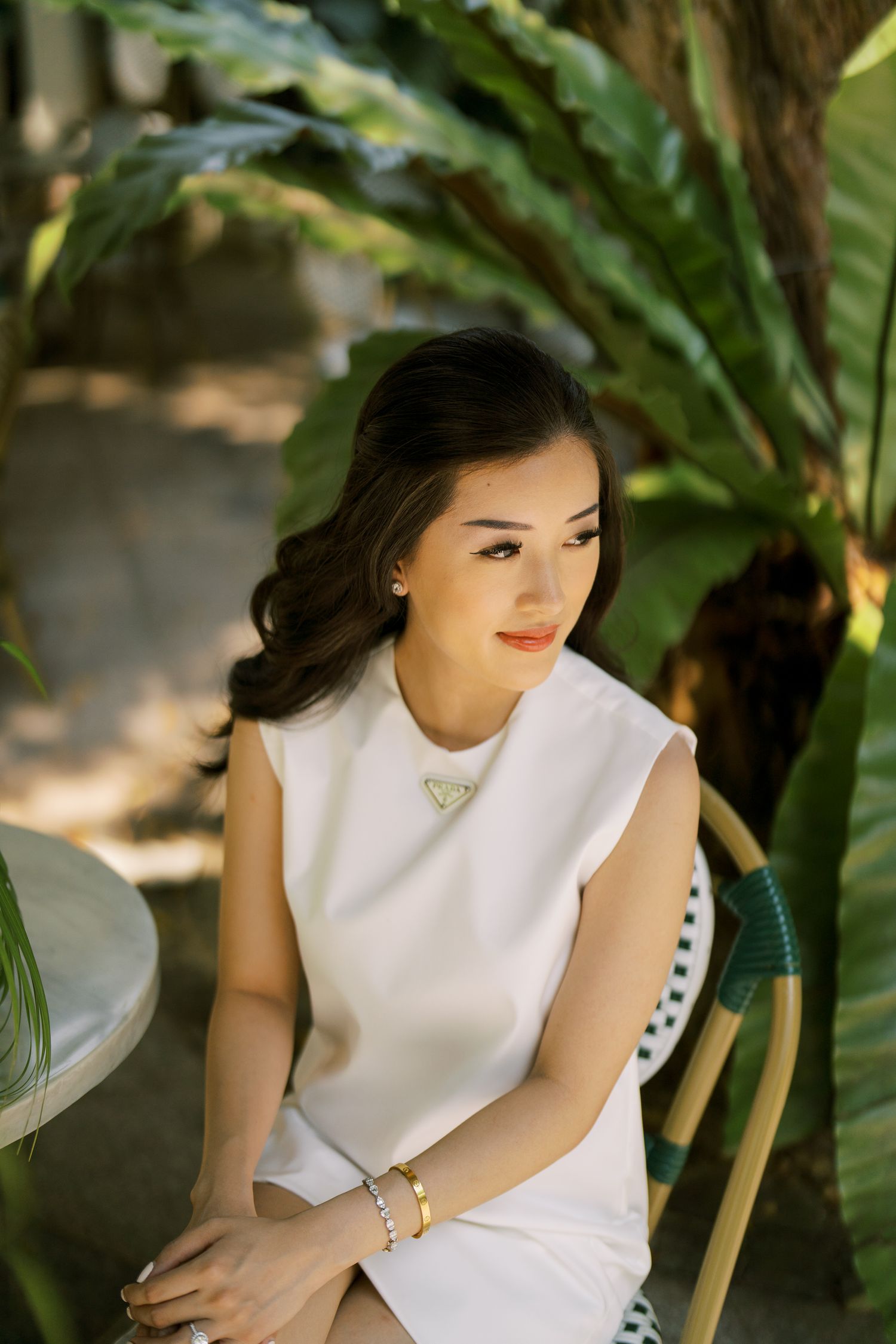 Person in elegant white sleeveless dress posed thoughtfully in a tropical garden setting.