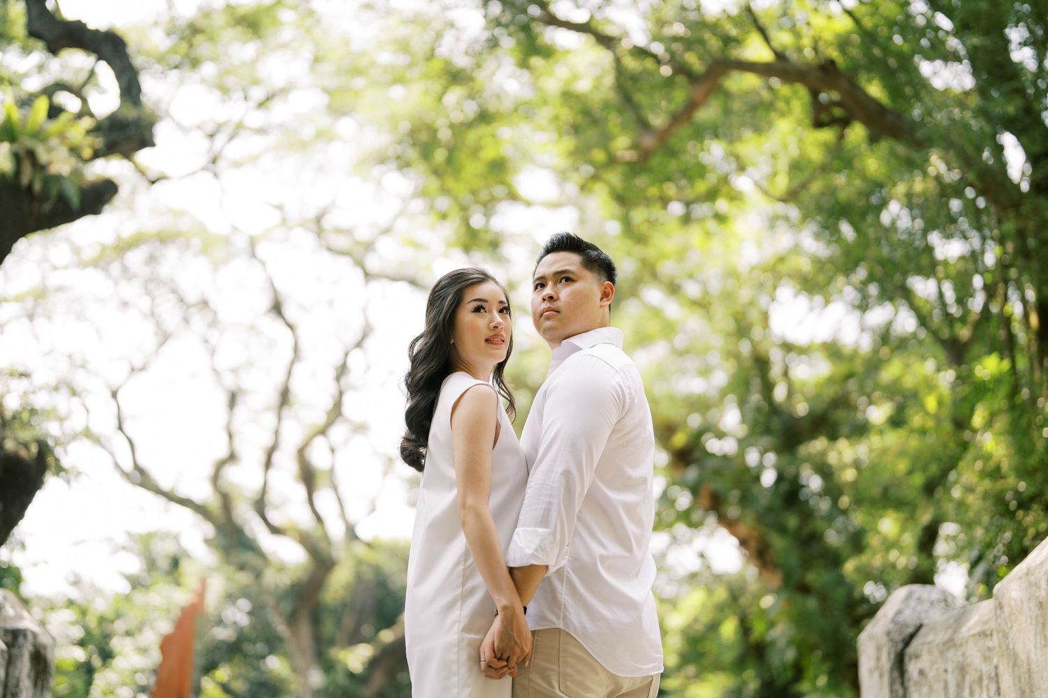 Intimate outdoor photoshoot with sunlight filtering through green trees in a natural setting.