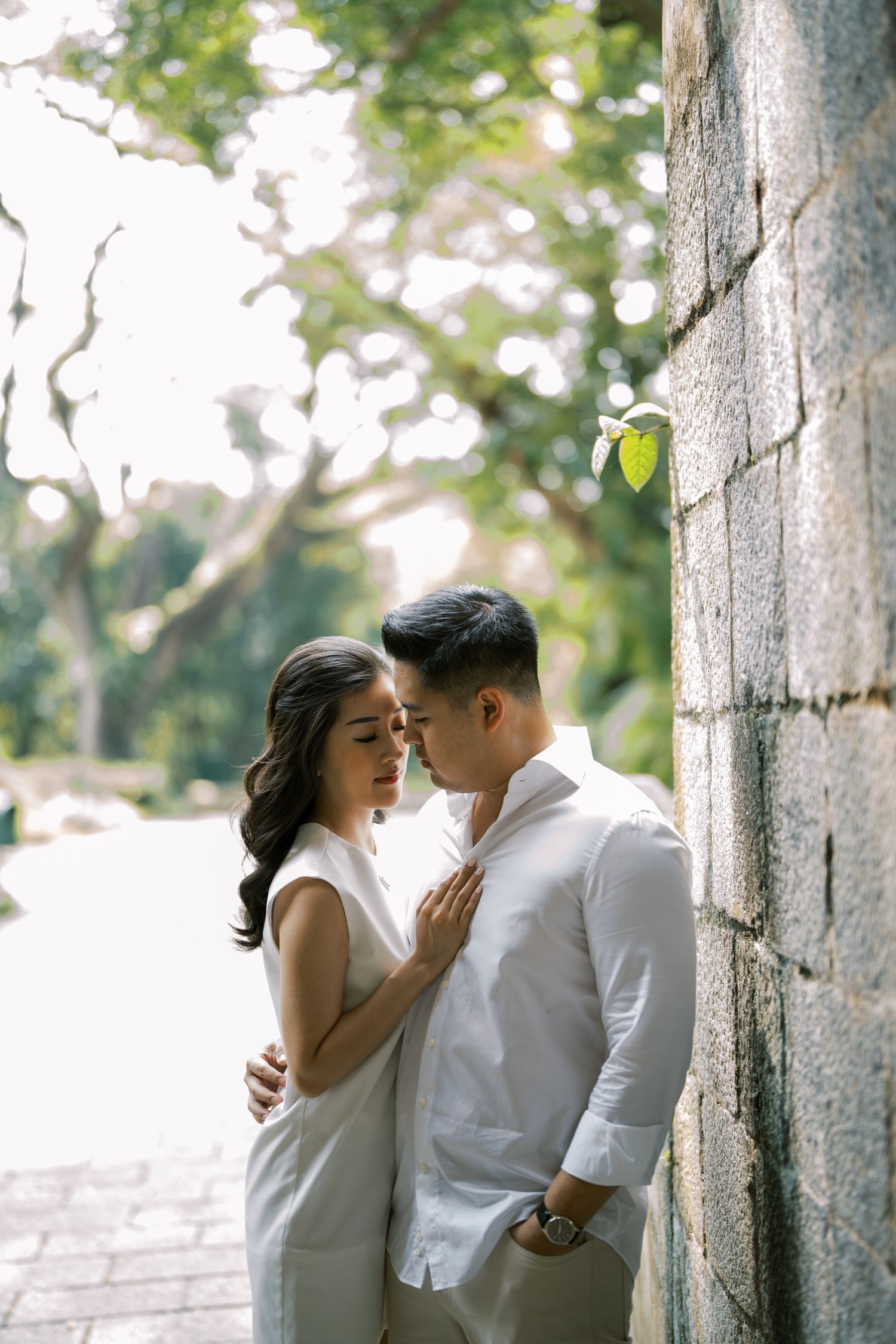 Intimate moment captured against stone wall backdrop with soft natural lighting.