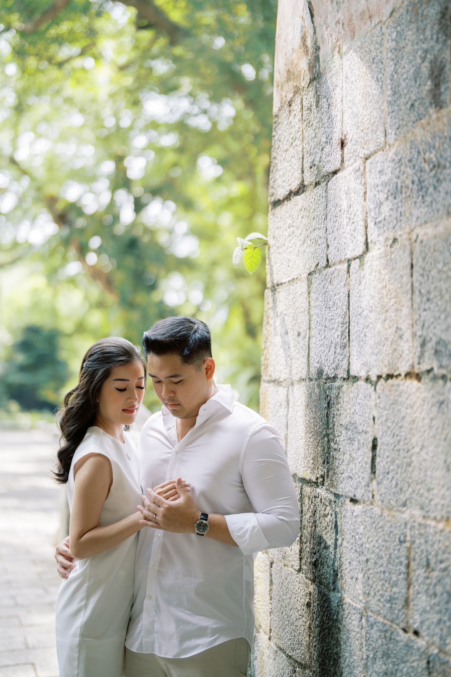 Couple sharing intimate dance poses against stone wall in natural lighting.