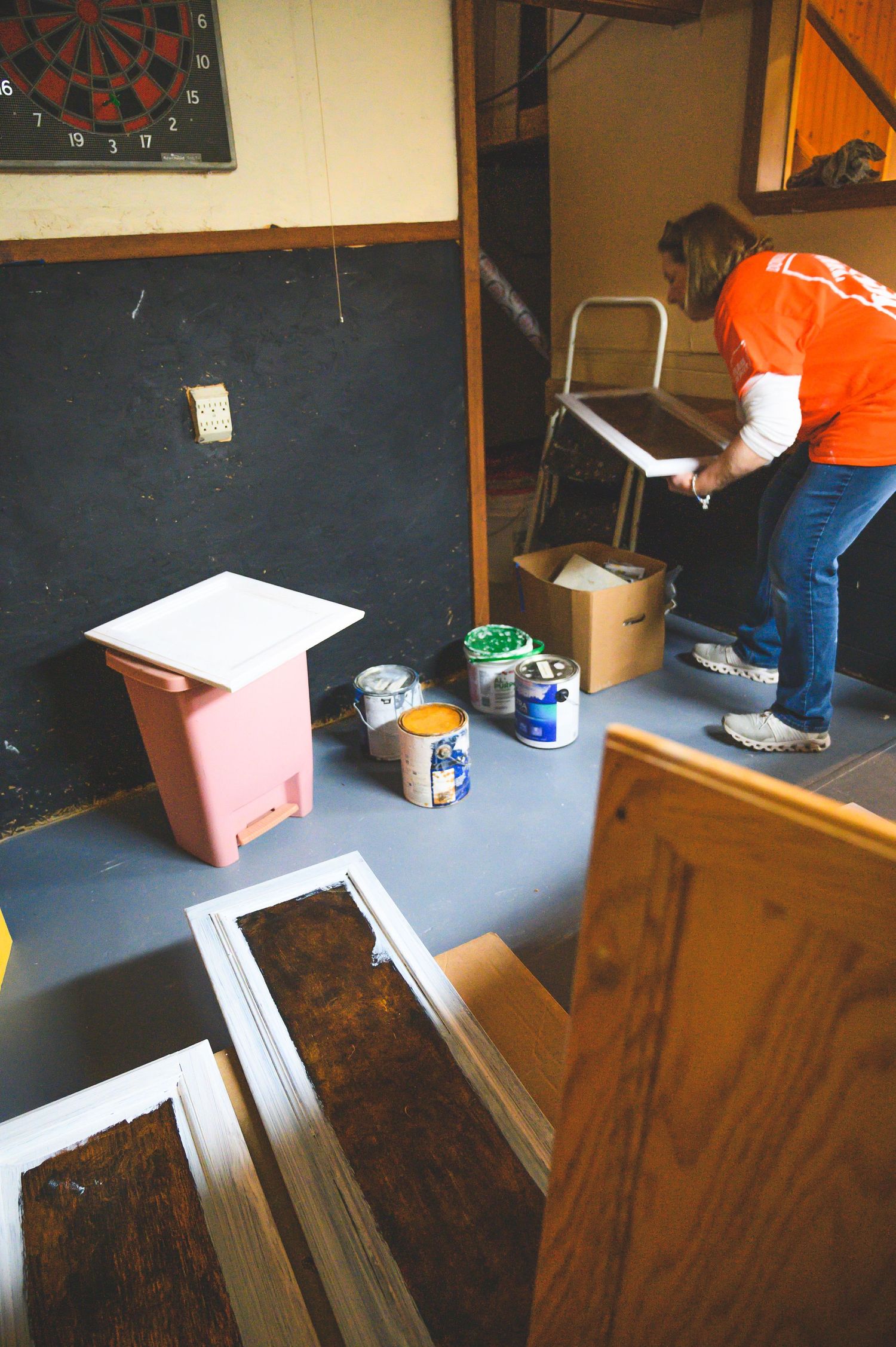Volunteer organizing materials and supplies in a basement workspace with paint cans visible.