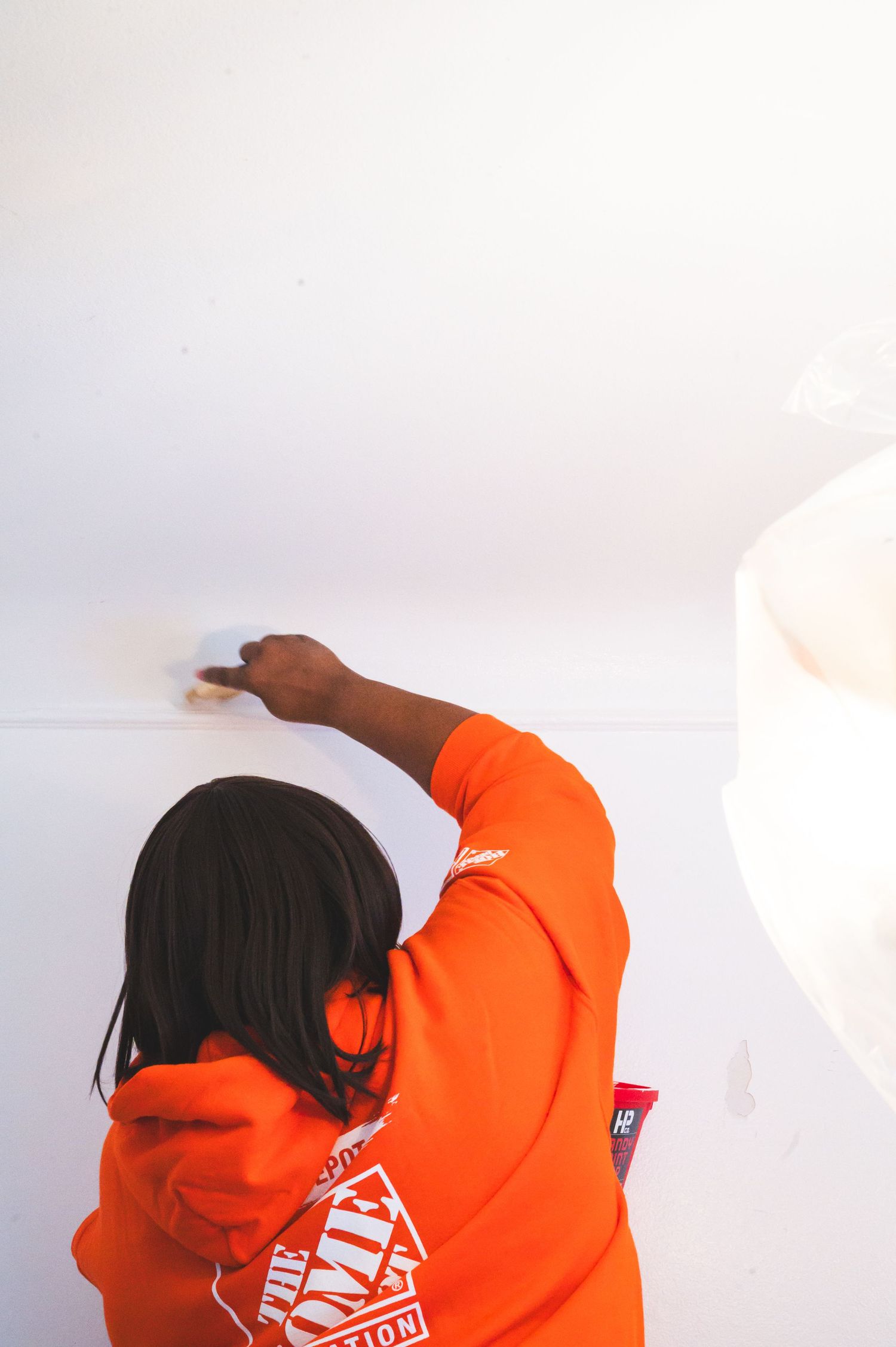 Volunteer in orange Home Depot shirt painting a white ceiling.